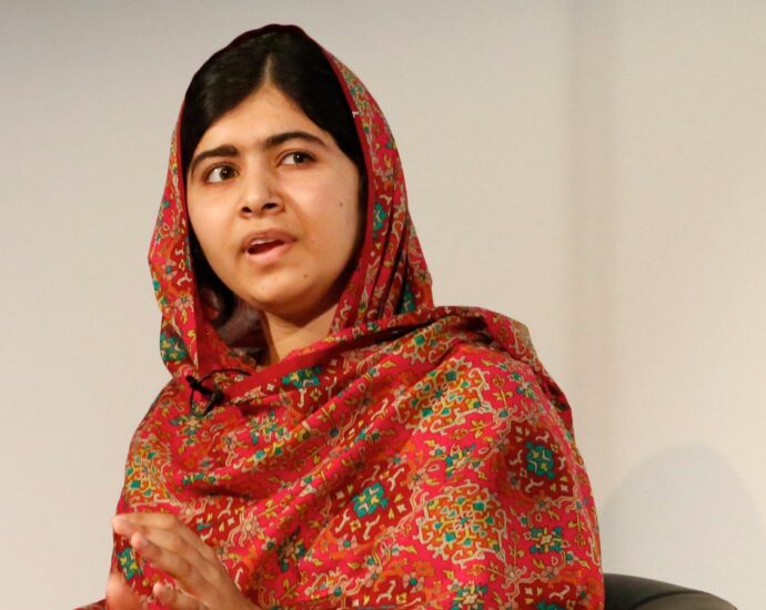 Photo of Malala Yousafzai sitting in a chair, looking off to the side, wearing a red and green patterned dupatta