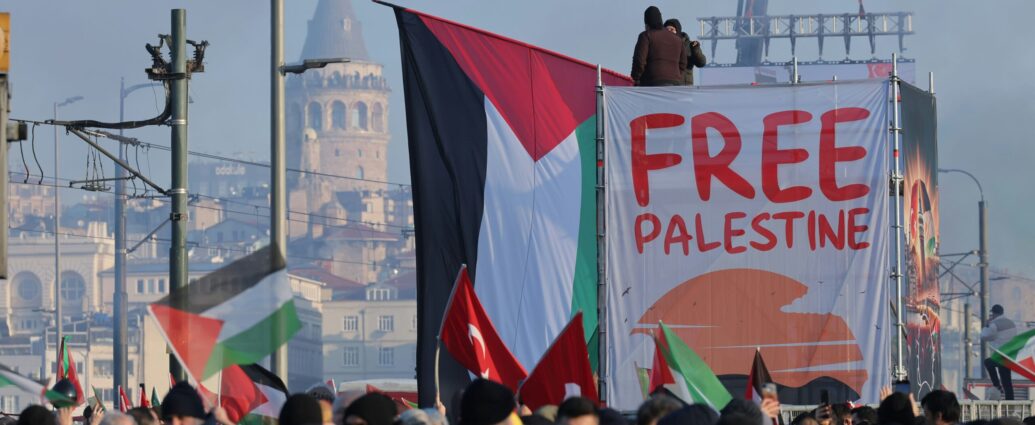 Photograph of a protest with a large Palestinian flag and free Palestine sign beside it