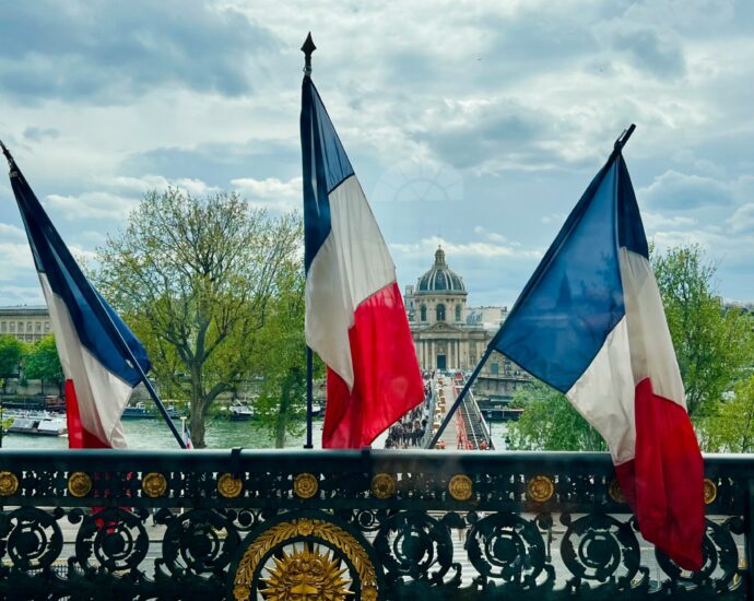 Three french flags sit upright from a balcony overlooking Paris.