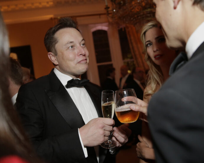 Photo of Elon Musk at an event, raising a drink towards another person